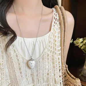 Dettaglio di una collana con ciondolo a fragola in resina bianca con cristalli su una modella.