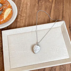 Dettaglio di una collana con ciondolo a fragola in resina bianca con strass su vassoio.