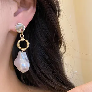 Primo piano di eleganti orecchini a goccia d'oro con una perla barocca su una modella asiatica.