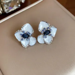 Close-up detail of exquisite white enamel flower stud earrings with elegant blue gemstones
