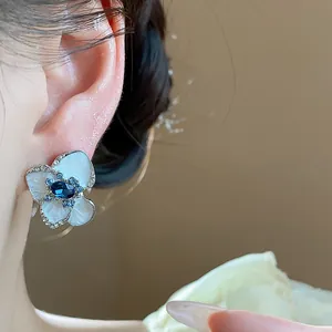 Macro detail of a white enamel flower stud earring with blue crystal center on ear