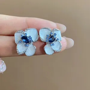 Detailed view of white enamel flower stud earrings with blue crystals and silver needles.