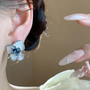 Close-up of elegant flower stud earrings with white enamel petals and a blue gemstone