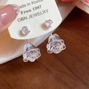 Nahaufnahme von herzförmigen Zirkonia-Steckern mit klaren Harz-Rosen-Ohrringen.