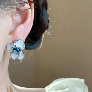 Detailed close-up of elegant flower stud earring with blue crystal and white enamel finish