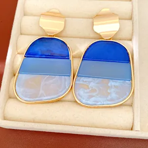 Dettaglio di orecchini a perno in acrilico blu con finiture geometriche dorate