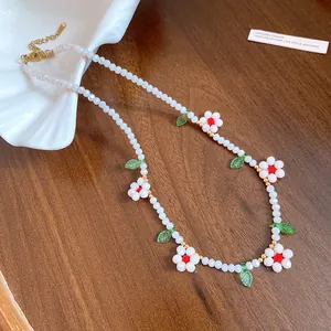 Detail view of white beaded necklace with red flower and green leaf charms on wood.
