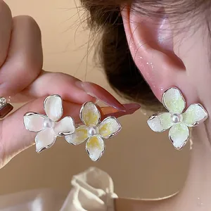 Primer plano de pendientes de flores esmaltadas de estilo francés con perla central blanca