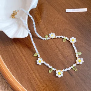 Macro view of dainty white resin flower beads and green leaf charms on a beaded necklace