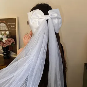 Elegant white fabric bow hair clip with long mesh streamers worn by a female model