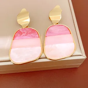 Dettaglio macro di orecchini geometrici con gocce in acrilico rosa e finitura metallica oro.