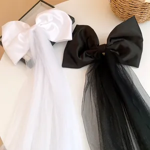 Close-up of black and white satin bow hair clips with long tulle veils on a white surface.