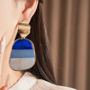 Primo piano di grandi orecchini in acrilico blu con parte superiore in metallo dorato