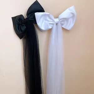 Detail of large black and white satin bow hair clips with long mesh tassels.