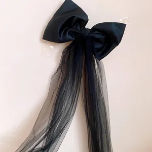 Close-up detail showing the texture of black fabric bow and long mesh tassels hair clip.