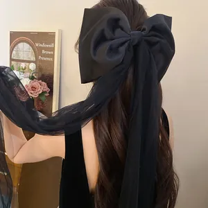 Elegant black fabric bow hair clip with mesh tassels shown on a model's hair