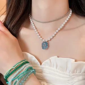 Primo piano della collana con ciondolo a uva blu e braccialetti di perline sul modello.