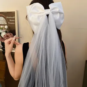 Detailed close-up showing the texture of a white satin bow hair clip with long elegant mesh veil