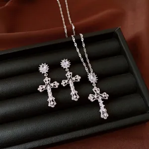 Detail van een sierlijke zilverkleurige kruishanger en oorbellen set met zirkoon.