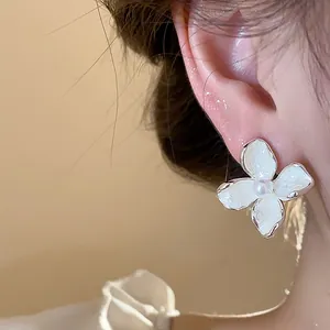 Primer plano detallado de un elegante pendiente de flor esmaltado blanco con una perla