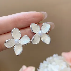 Vista macro detallada de pendientes de flor en esmalte blanco con una perla central fina