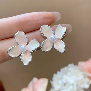 Primer plano de delicados pendientes de flor en esmalte con perlas centrales en la mano.