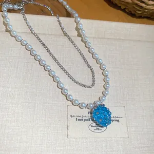 Dettaglio ravvicinato della collana a doppio strato con perle bianche e ciondolo a uva blu.