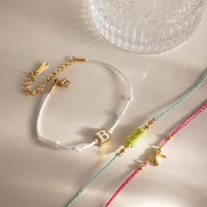 Gros plan sur trois bracelets empilables en cordon avec lettre B dorée et noeud