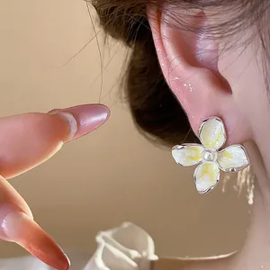 Primer plano detallado de elegantes pendientes de flor de esmalte con perla blanca