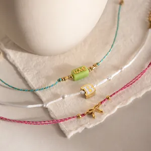 Détail macro de bracelets en cordon empilés avec perle LOVE, initiale B et nœud doré