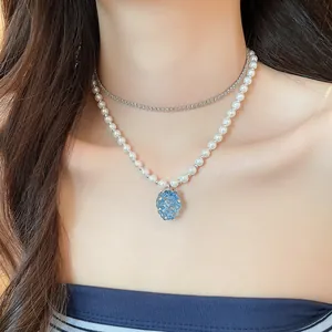 Dettaglio di un ciondolo a grappolo d'uva blu su una collana di perle bianche a due strati