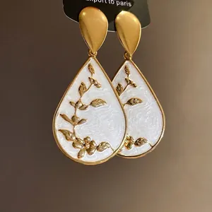Elegant gold teardrop earrings featuring white enamel and intricate floral branch patterns