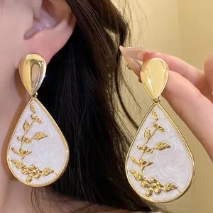 Detailed close-up of gold water drop earrings featuring white floral enamel design.