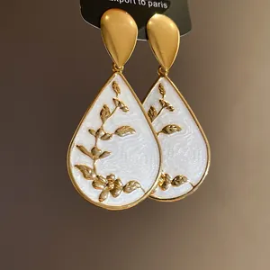Detailed close-up of elegant waterdrop earrings with white enamel and gold floral patterns