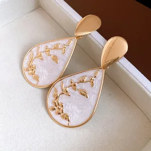 Close-up of vintage gold water drop earrings with white enamel and floral pattern.