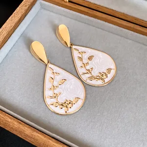 Close-up detail of retro teardrop earrings with gold floral patterns on white enamel inlay