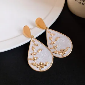 Close-up view of elegant waterdrop earrings with gold floral relief and white enamel finish.
