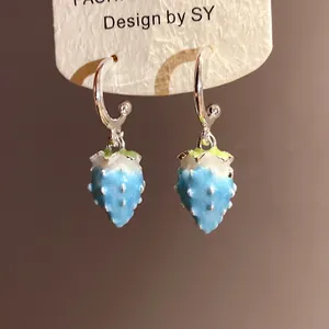 Detailed shot of blue enamel strawberry dangle earrings hanging from silver hoop hooks