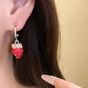 Close-up detail of sweet red enamel strawberry pendant earring worn by a model