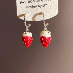 Close-up of cute enamel strawberry pendant earrings with red and white finish