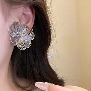 Gros plan d'une boucle d'oreille fleur en métal argenté avec une perle sur l'oreille.