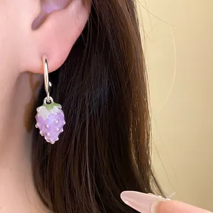 Close-up of a purple strawberry pendant earring with silver needle on a model's ear