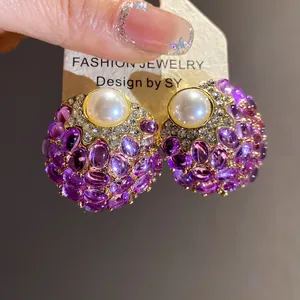 Primer plano de pendientes vintage con perla blanca y piedras preciosas moradas