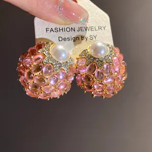 Detalle de pendientes vintage redondos con piedras rosas y una perla central