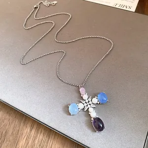 Close-up of a silver cross pendant necklace with pastel resin stones and white pearls