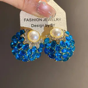 Primer plano detallado de pendientes vintage azules con una perla blanca en el centro