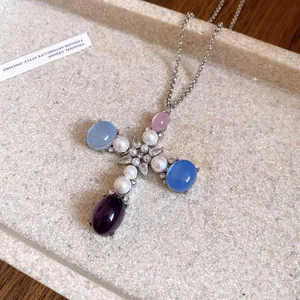 Close-up of elegant cross pendant featuring resin stones, pearls, and zircons
