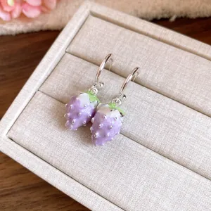 Detailed close-up of purple enamel strawberry drop earrings on a beige jewelry display tray