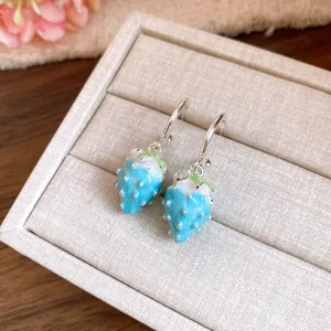 Detail shot of light blue strawberry earrings with enamel finish in a beige jewelry box