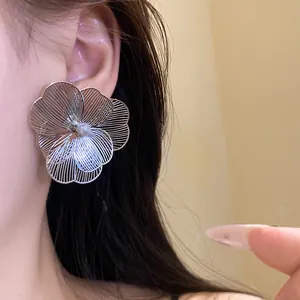 Close-up detail of a silver metal flower earring with a pearl center worn on the ear